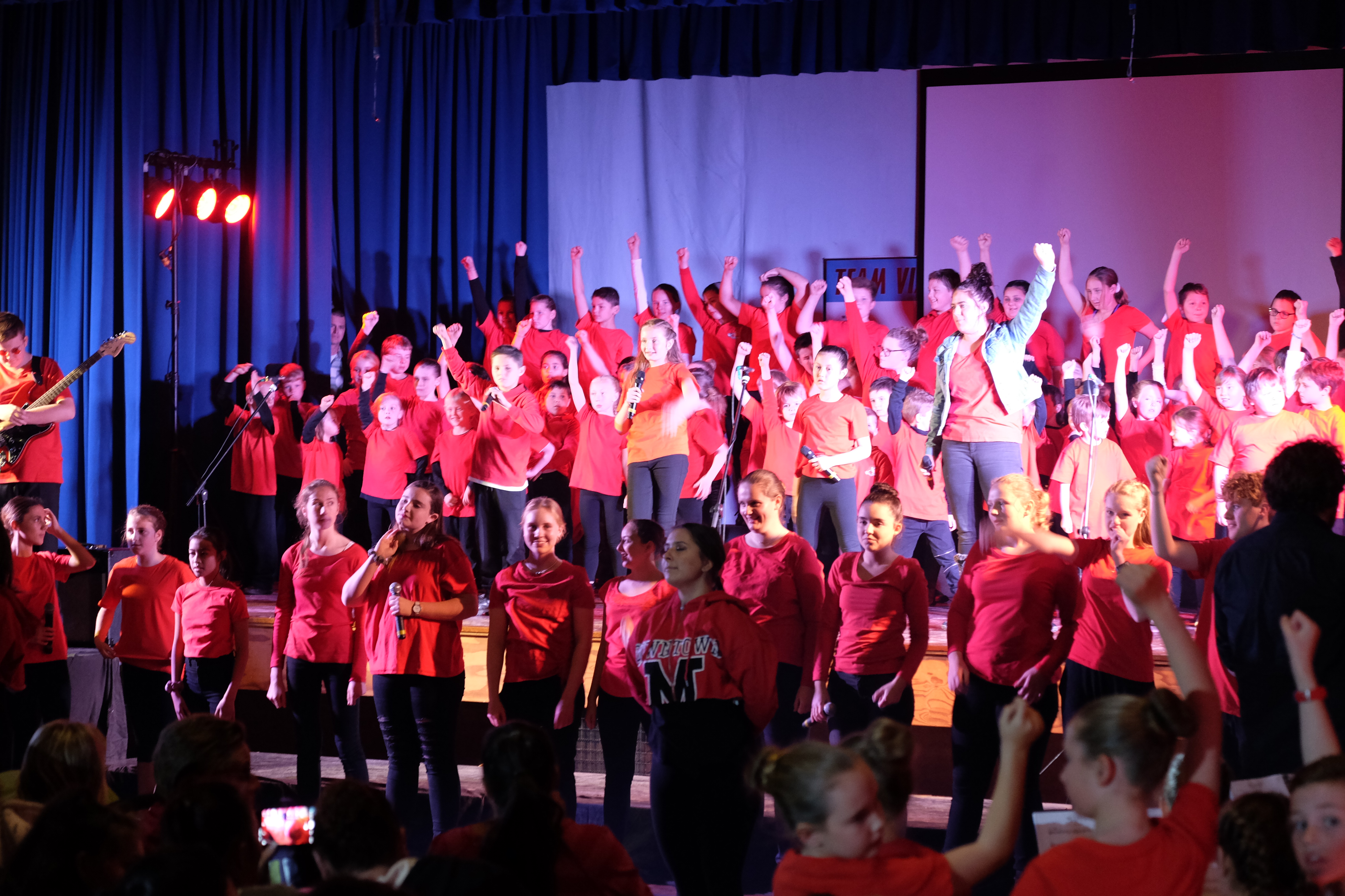 large group of students on stage in red tshirts posing for the audience