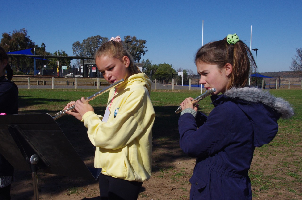 2 student playing flute outdoors on an oval