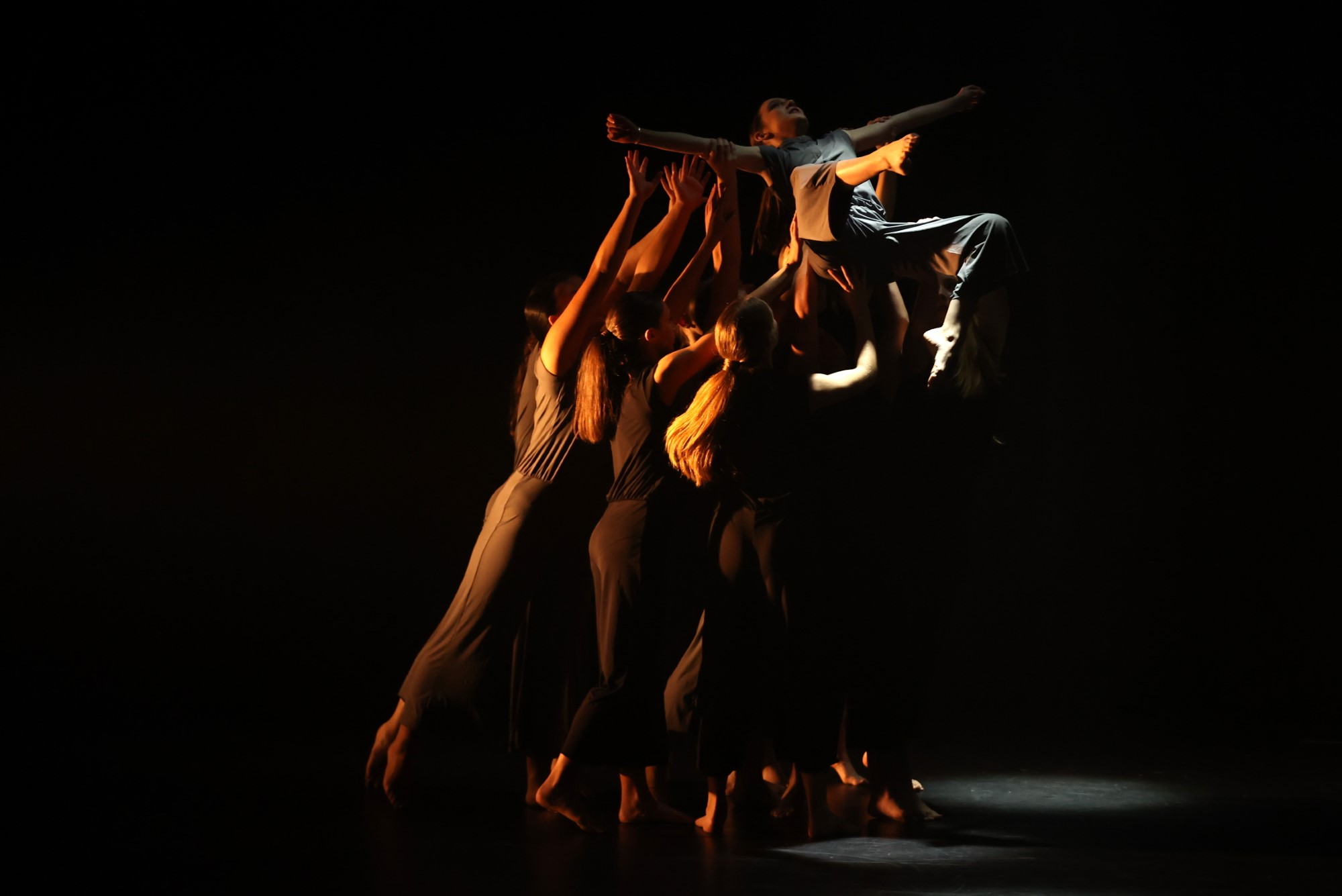 A group of dancers with arms outstretched holding up a single dancer 