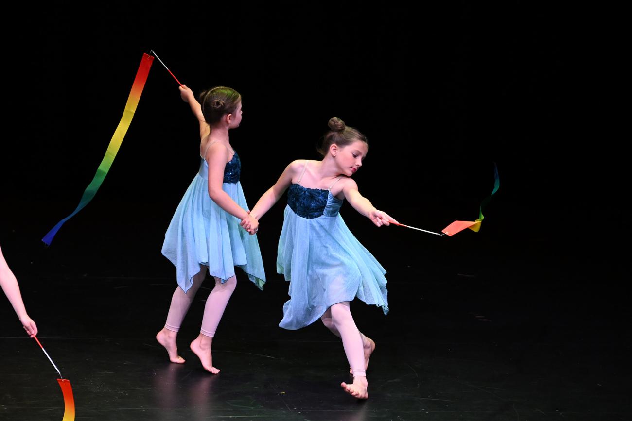 2 dancers in blue dresses holding hands dancing in a circle with ribbons