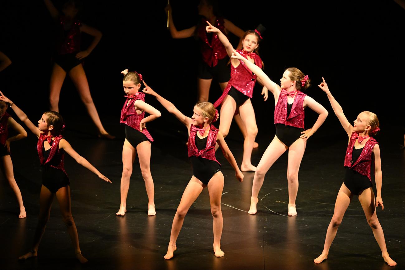 dancers on stage in black leotards and pink vest in disco pose