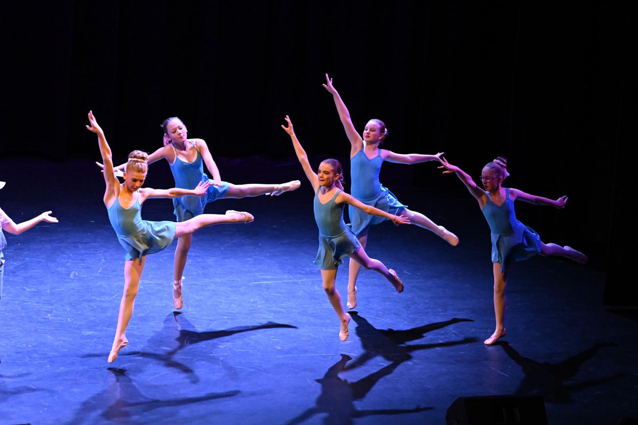 5 young dancers in blue leotards and ballet shoes in arabesque