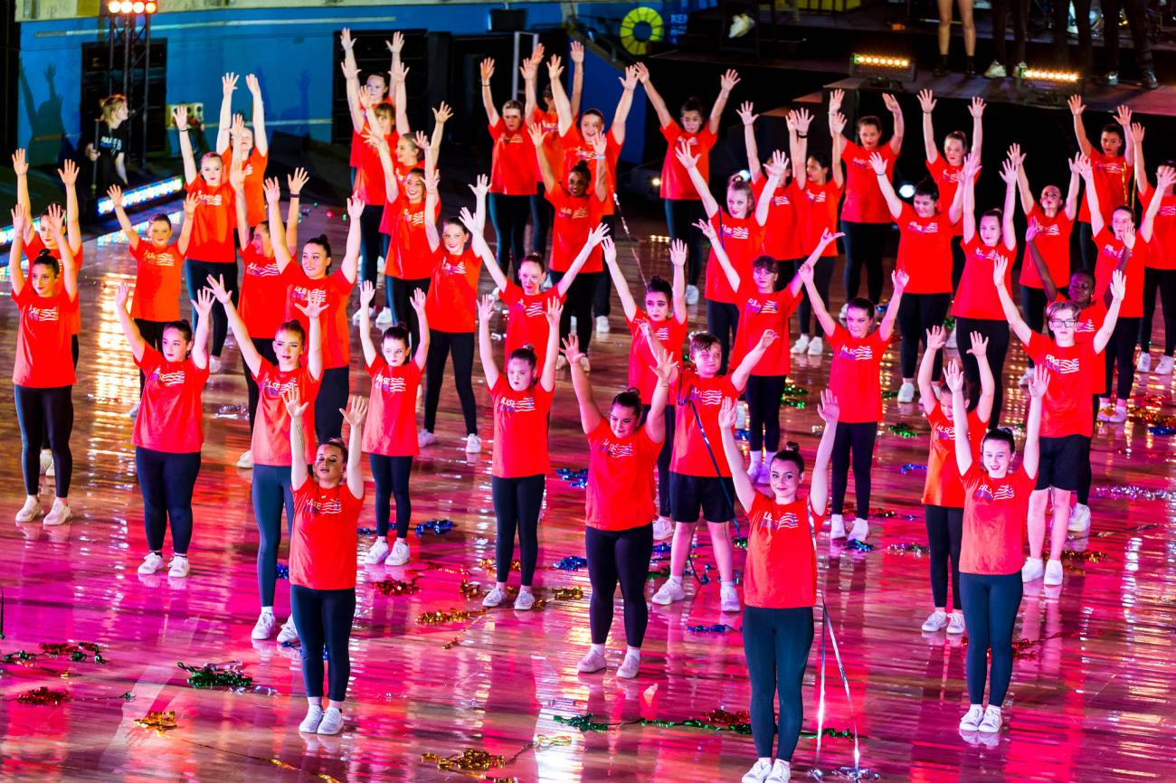 student dancers on stage with arms up in air wearing red tshirts