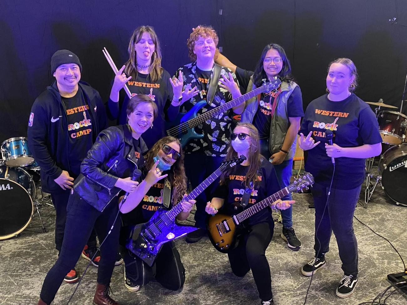 A group of students and staff dressed in black rock camp t shirts and black pants posing with their electric instruments