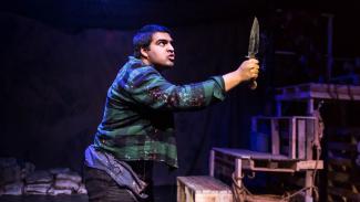 An actor playing Macbeth wearing modern clothing and holding a dagger