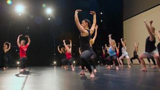 A dance class with teacher and students in a deep second plie with arms above head
