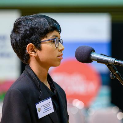 2023 Senior Premier's Spelling Bee State Finals champion, Trilok Shenoy, stands in front of a microphone to spell a word.